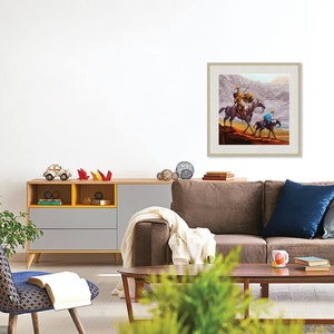 May include: A framed painting of two people on horseback riding through a desert landscape. The painting is in a light brown frame and is hanging on a white wall.