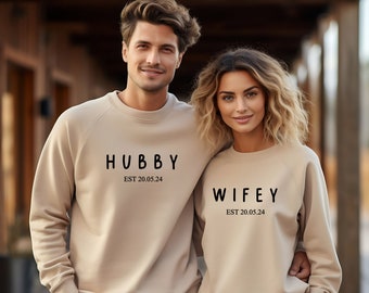 May include: A couple wearing matching beige sweatshirts with the text "Hubby Est 20.05.24" and "Wifey Est 20.05.24" printed on them.