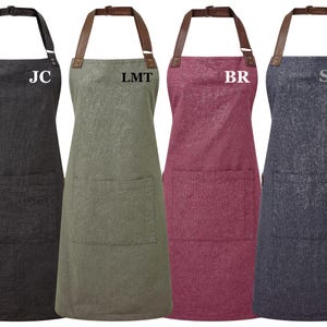 Puede incluir: Cuatro delantales de diferentes colores con correas ajustables y un bolsillo grande. Los delantales están personalizados con las iniciales "JC", "LMT", "BR" y "SM".