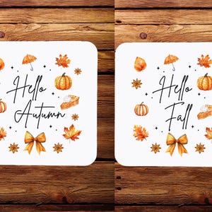 Puede incluir: Dos posavasos blancos con diseños de otoño. El posavasos de la izquierda presenta el texto "Hello Autumn" con ilustraciones de calabazas, hojas y una tarta. El posavasos de la derecha presenta el texto "Hello Fall" con ilustraciones similares.