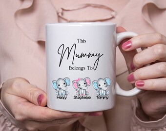 Può includere: Tazza in ceramica bianca con il testo "This Mummy Belongs To" e tre elefanti dei cartoni animati con i nomi Henry, Stephanie e Tommy.
