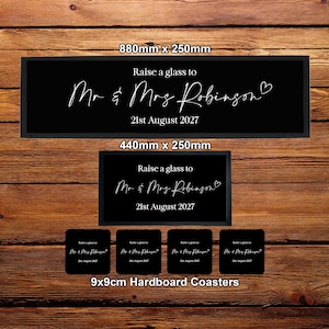 May include: A black bar runner measuring 880mm x 250mm, a smaller runner measuring 440mm x 250mm, and four 9x9cm hardboard coasters. All items feature the white text "Raise a glass to Mr & Mrs Robinson" with a heart icon and "21st August 2027".