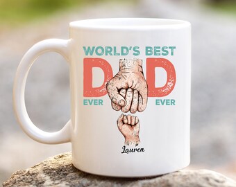 May include: White ceramic mug with a red and blue design that says "World's Best Dad Ever" with a father and child's hands clasped together. The name "Lauren" is printed below the hands.