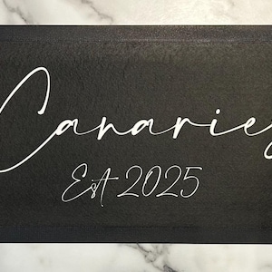 May include: Black sign with white text that reads "The Canaries Inn Est. 2025".