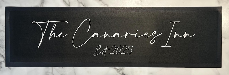 May include: Black sign with white text that reads "The Canaries Inn Est. 2025".