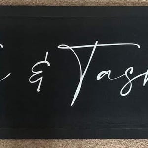 May include: Black rectangular sign with white cursive text that reads "Tom & Tasha's".