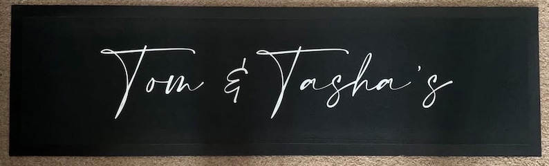 May include: Black rectangular sign with white cursive text that reads "Tom & Tasha's".