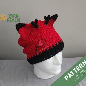 May include: Red and black crochet hat with a red eye design and antlers. The hat is on a white mannequin head. The text "PATTERN Printable Download File" is in green on a white background.