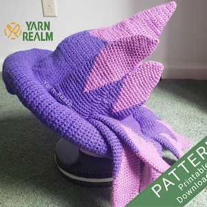 Puede incluir: Un gorro de crochet morado y rosa con una parte superior puntiaguda y una cola larga. El gorro está sentado sobre una superficie blanca y negra. El texto "PATTERN Printable Download File" está en la esquina inferior derecha de la imagen.