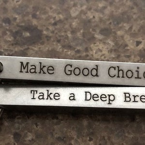May include: A silver keychain with two metal bars. The top bar reads "Make Good Choices" and the bottom bar reads "Take a Deep Breath".