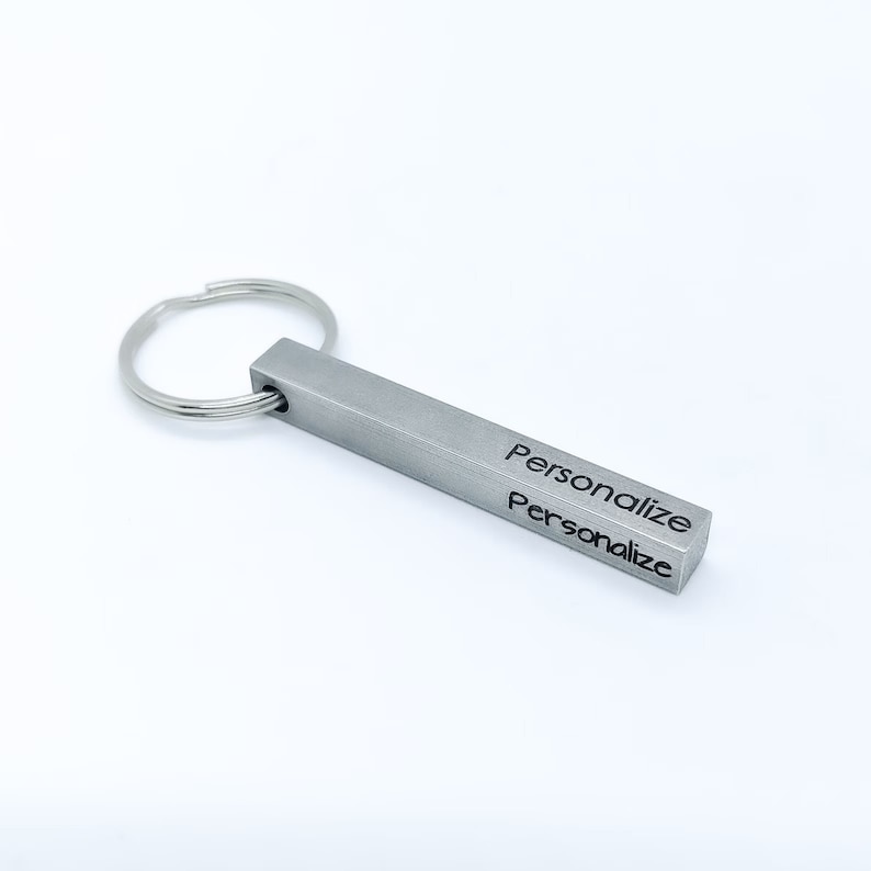 May include: A silver metal keychain with a rectangular bar that says "Personalize" on two sides. The keychain has a silver metal ring.