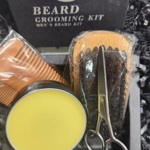 May include: A beard grooming kit with a wooden comb, brush, scissors, and a jar of beard balm. The kit is packaged in a black box with the words "Beard Grooming Kit" and "Men's Beard Kit" printed on it.