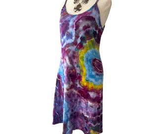 May include: A tie-dye sundress in shades of purple, blue, yellow, and green. The dress has a scoop neckline and spaghetti straps. A silver-toned necklace with circular pendants is also visible.