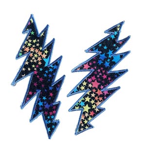 May include: Two embroidered lightning bolt patches. Each patch has a black background with colorful star patterns. The edges are outlined in a dark blue thread. The patches are set against a white background.