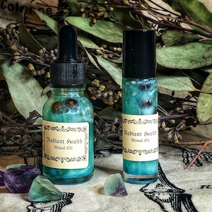 May include: Two glass bottles of "Radiant Health Ritual Oil" with teal liquid and black caps. One bottle has a dropper, the other a rollerball. The labels are cream-coloured with ornate borders. Fluorite crystals are scattered around the bottles.