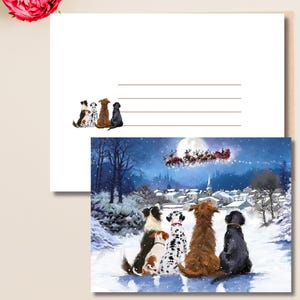 Op de afbeelding: Een kerstkaart met een aquarel illustratie van zes honden die kijken naar de slee van de kerstman die over een besneeuwd dorp vliegt onder een volle maan. De kaart bevat ook een blanco ruimte voor een boodschap en een rij honden.