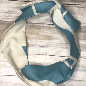 May include: A teal and white patterned headband. The headband is made of a soft, stretchy fabric and is tied in a knot at the top.