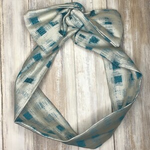 May include: A silver and teal patterned headband with a knotted design. The headband is made of a soft, stretchy fabric and is perfect for adding a touch of style to any outfit.