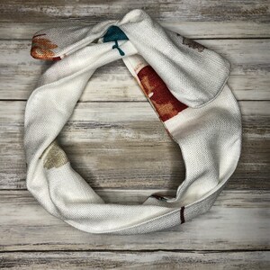 May include: White fabric headband with a colorful abstract pattern. The headband is tied in a knot at the top.