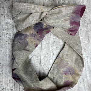 May include: A light gray linen headband with a knotted design and a purple and burgundy floral print.