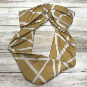 May include: A gold and white geometric patterned fabric headband. The headband is tied in a knot at the top.