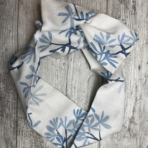 May include: A white fabric headband with a blue floral pattern. The headband is tied in a knot at the top.