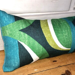 May include: A green, blue and white doorstop with a geometric pattern. The doorstop is made of fabric and is rectangular in shape.