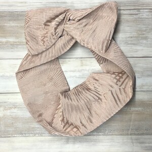 May include: A beige fabric headband with a knotted design and a subtle geometric pattern.