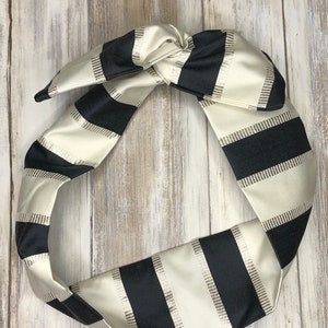 May include: A black and white striped headband made of satin fabric. The headband is tied in a knot at the top.
