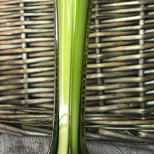 May include: A tall, green glass vase with a flared, star-shaped base. The vase has a glossy finish and a unique, angular design.
