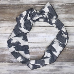 May include: A white and gray patterned headband with a knotted design. The headband is made of a soft, stretchy fabric.