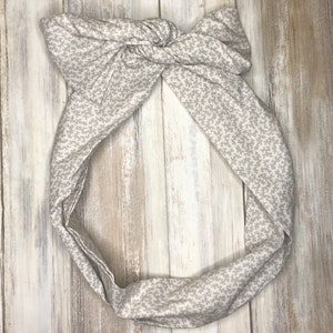May include: A white headband with a gray floral pattern. The headband is tied in a knot at the top.
