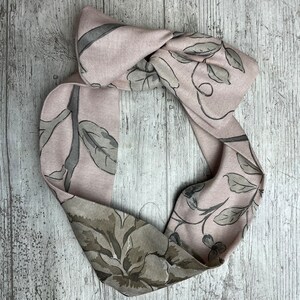 May include: A pink fabric headband with a floral pattern in shades of gray. The headband is tied in a knot at the top.