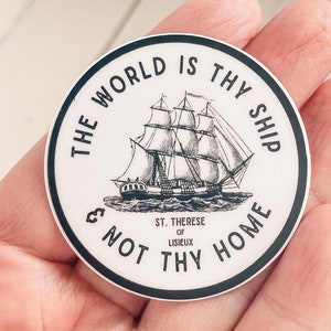 May include: A black and white sticker with a quote from St. Therese of Lisieux: "The world is thy ship & not thy home". The quote is surrounded by a circle with a ship illustration in the center.