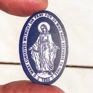 以下が含まれることがあります： 聖母マリアの白い画像と「O Mary Conceived Without Sin Pray For Us Who Have Recourse To Thee 1830」というテキストが書かれた青い楕円形の宗教メダルです。