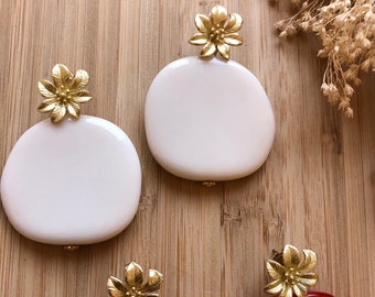 May include: A pair of statement earrings with large round white and orange resin pieces. Each piece has a gold flower charm on top.