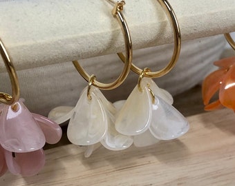 May include: Gold hoop earrings with white flower-shaped charms dangling from the bottom.