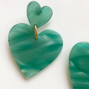 May include: A pair of green heart-shaped earrings with a gold accent. The earrings are made of a marbled material.