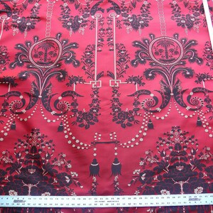 May include: Red fabric with a black and white floral pattern. The pattern features a repeating design of a chandelier with a beaded chain and a palm tree in a circle.