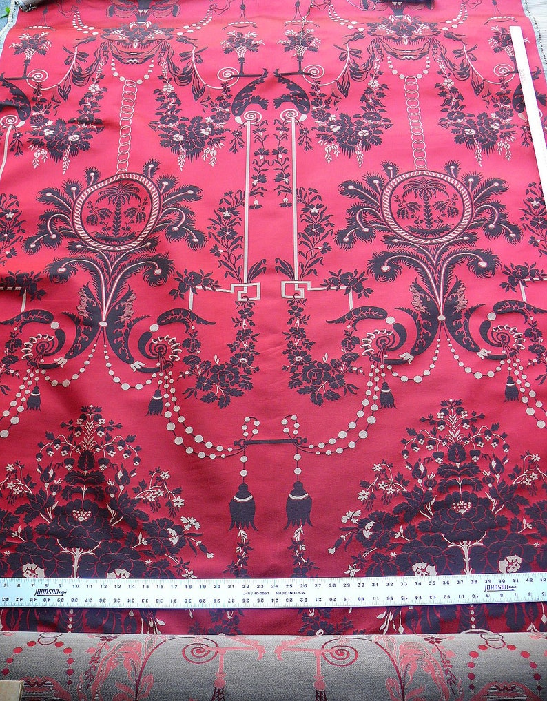 May include: Red fabric with a black and white floral pattern. The pattern features a repeating design of a chandelier with a beaded chain and a palm tree in a circle.