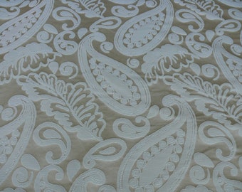May include: White paisley pattern on a beige fabric background. The pattern is embossed and has a raised texture.