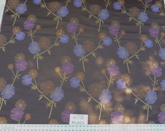 Può includere: Un tessuto marrone con un motivo ripetitivo di fiori viola e blu. Il tessuto ha una leggera lucentezza e una superficie testurizzata. Il tessuto è etichettato "678 MISCHIEF".