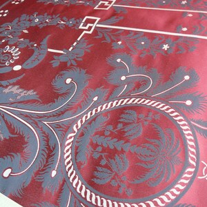 May include: Close-up of a red fabric with a white and gray floral pattern. The fabric has a textured, woven look and features a repeating design of stylized flowers and leaves.