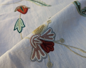 Könnte beinhalten: Nahaufnahme eines bestickten Stoffes mit einem floralen Muster. Der Stoff ist weiß mit beige, brauner, roter und grüner Stickerei. Die Stickerei zeigt eine Blume mit einer roten Mitte und rosa Blütenblättern.