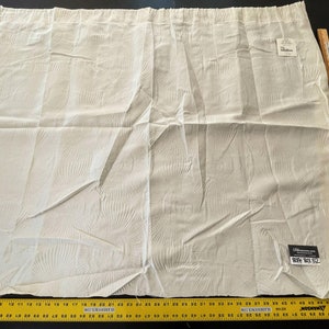 May include: A folded, cream-colored curtain panel with a textured, fan-like pattern. The curtain has a label with text and is next to a wooden ruler. The ruler is marked with centimeters and the text "THE HOME DEPOT".