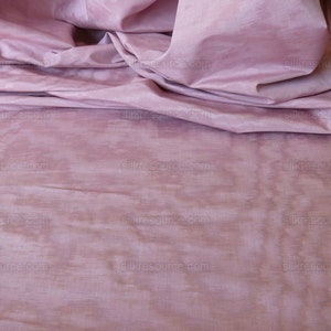 May include: A close-up of a soft, pink fabric with a smooth, silky texture. The fabric is draped in folds, creating a luxurious and elegant look.
