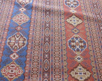 May include: A close-up of a fabric with a repeating pattern of blue, red and brown geometric shapes. The fabric has a woven texture and a traditional design.
