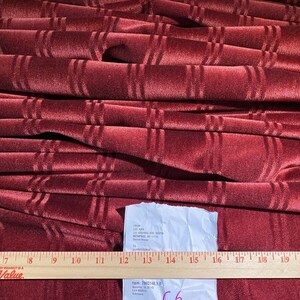 May include: A close-up of a burgundy velvet fabric with a subtle striped pattern. The fabric is folded and stacked, and a ruler is visible in the bottom of the image.