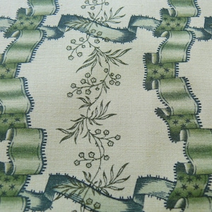 May include: A cream-colored fabric with a repeating pattern of green ribbons and stylized floral sprigs. The ribbons are edged in black and have a star-like pattern.