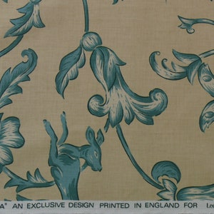 May include: A beige fabric with a teal floral pattern. The pattern includes stylized flowers, leaves, butterflies, and a deer. The fabric has the text "DAMBURA' AN EXCLUSIVE DESIGN PRINTED IN ENGLAND FOR Lee Jofa INC."